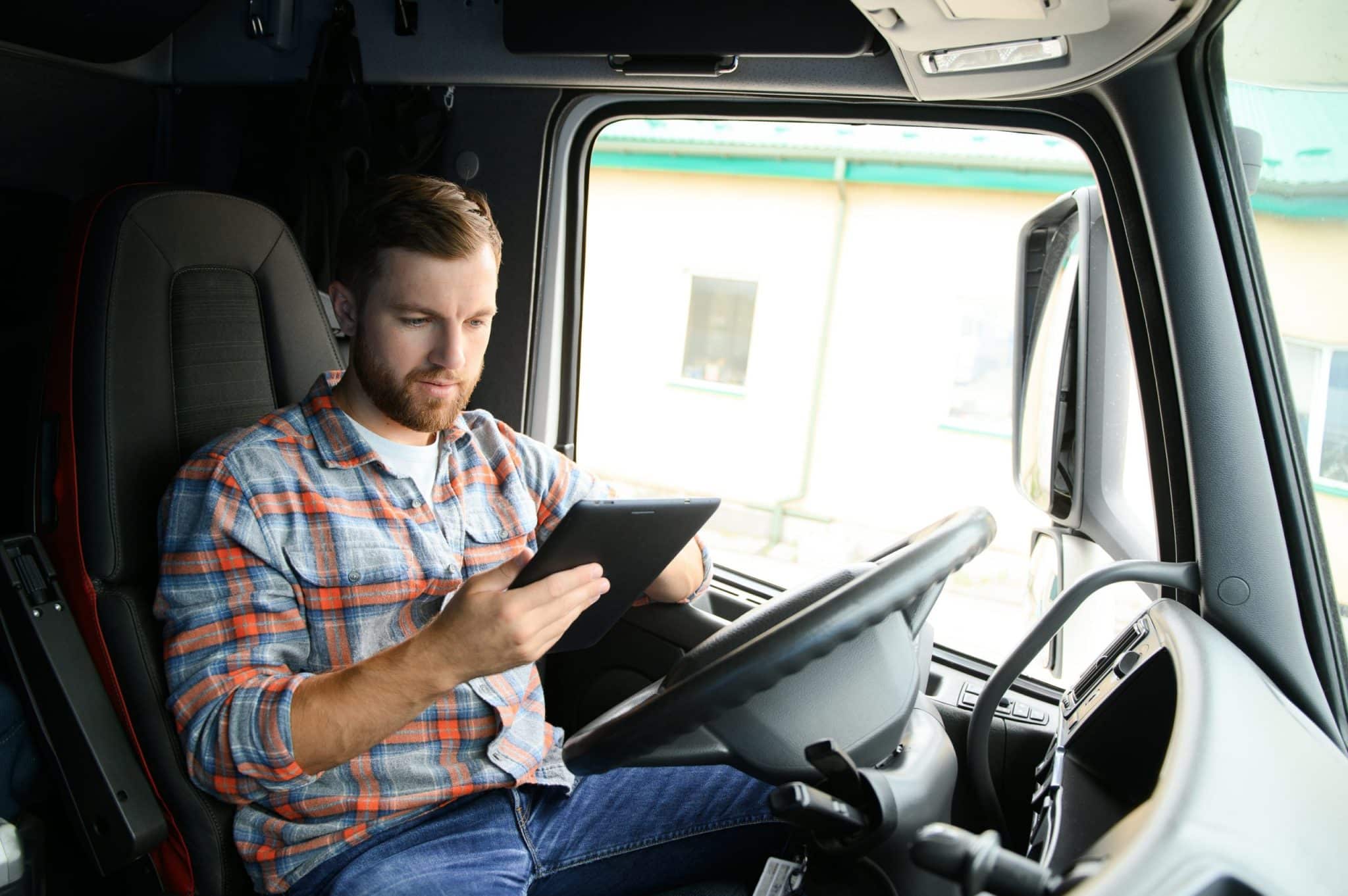 Man truck driver sitting behind wheel of car and holding digital tablet in his hands